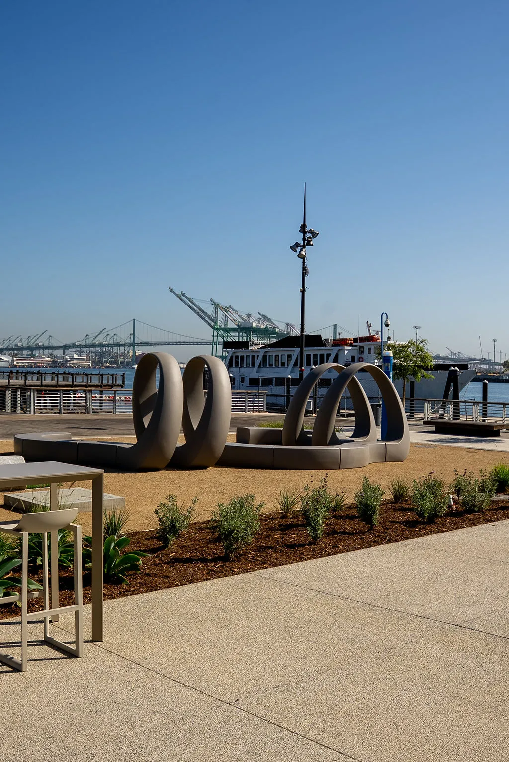 Harbor-edge seating and sculpture with port cranes behind